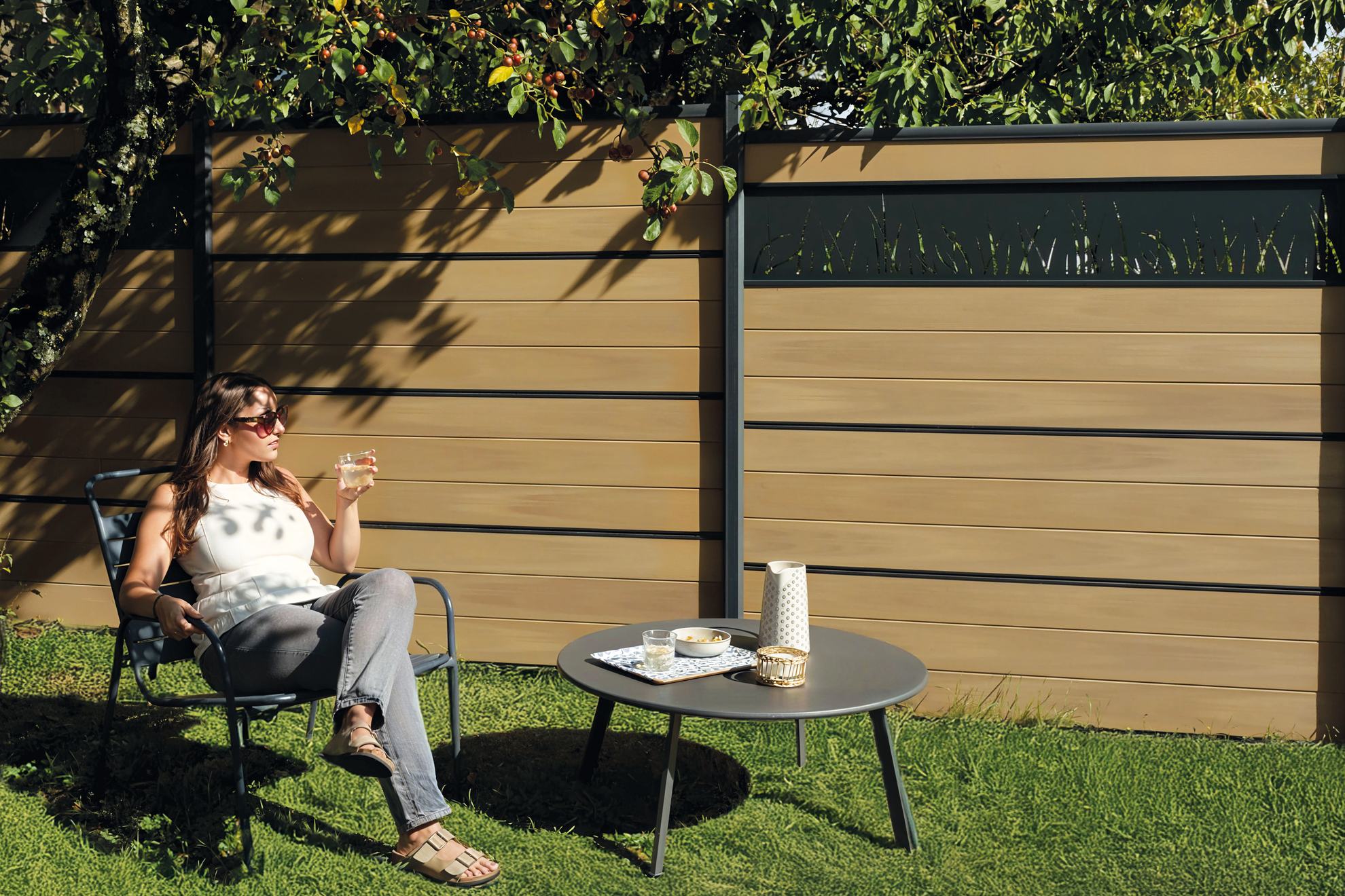 Cloture composite Atmosphère coulelur Nuances chêne clair transat avec jeune femme verre à la main