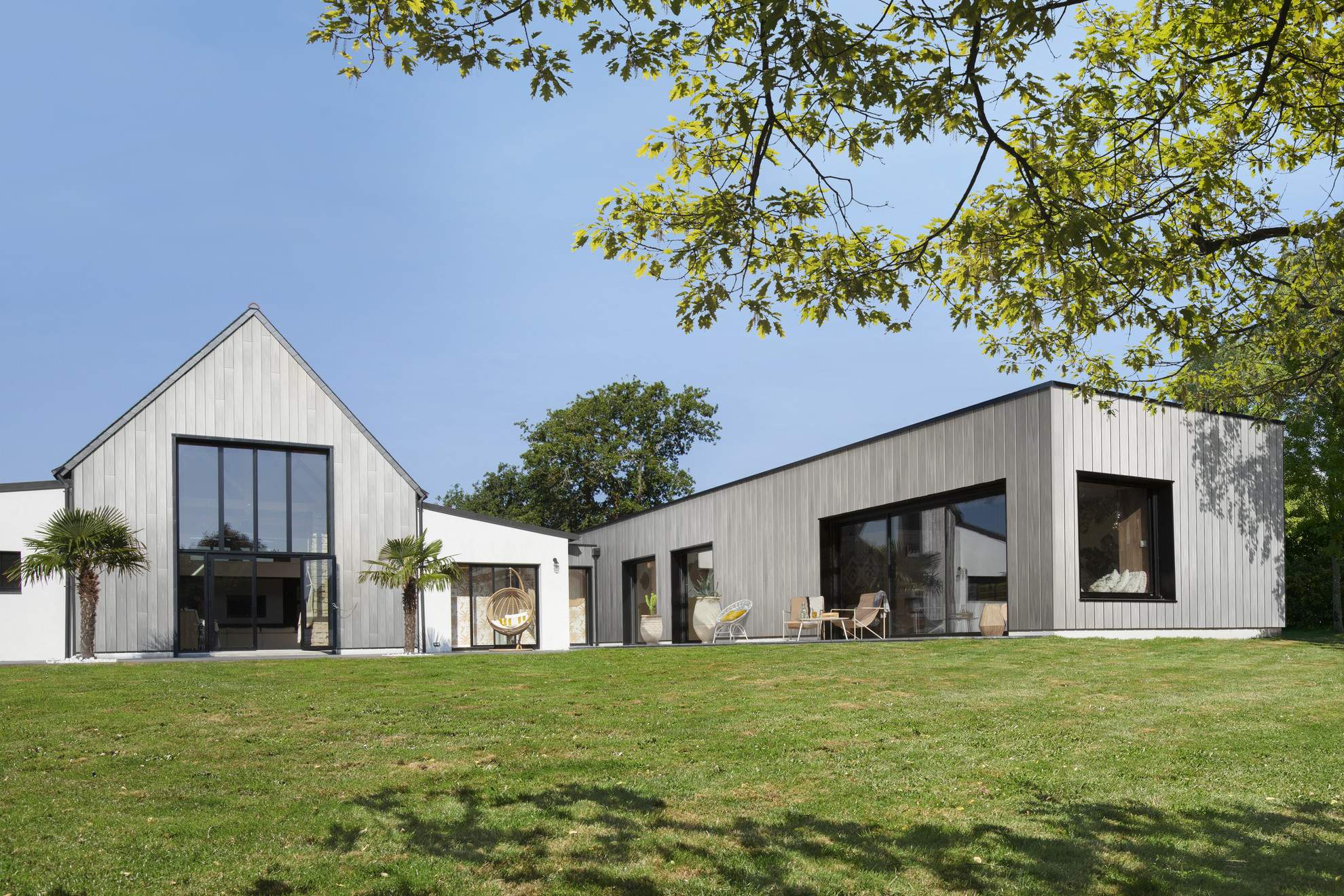 Casa contemporanea con rivestimento in legno composito Silvadec, composta da due volumi distinti con tetto a spiovente e tetto piano, circondata da un giardino verdeggiante